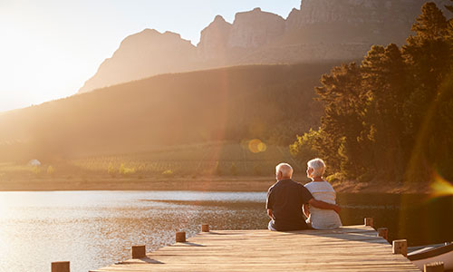 Couple sitting on the end of a dock looking out over a lake with mountains in the background