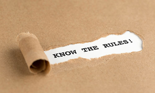 A piece of brown paper is ripped on rolled back to reveal the words "Know the Rules!"