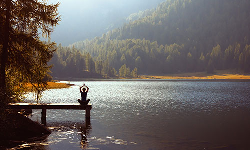 Woman practising yoga at the end of a dock on a lake in a mountain valley